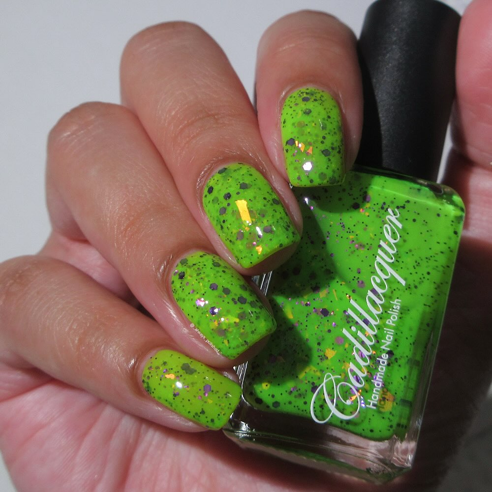 Dapper but no Dan by Cadillacquer, neon lime green glitter flakie with purple glitter and orange-yellow iridescent flakes under direct flash, bottle held in a light-medium hand