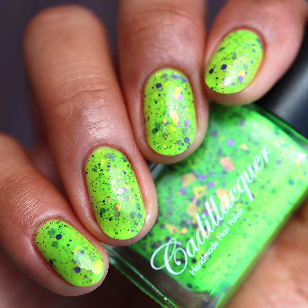 Dapper but no Dan by Cadillacquer, neon lime green creme with purple glitter and orange-yellow multichrome flakies, bottle held in a medium-deep hand