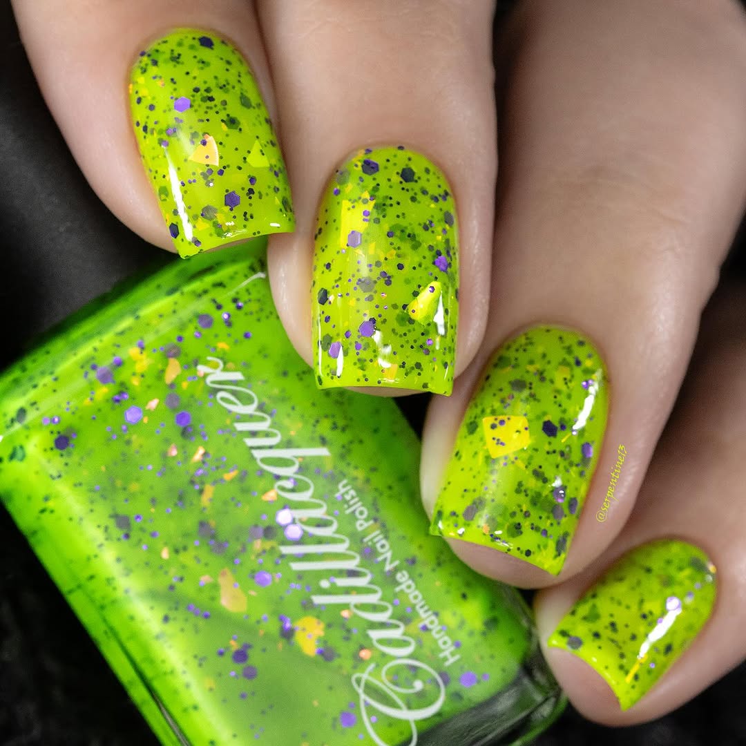 Dapper but no Dan by Cadillacquer, neon lime green glitter flakie with mixed-size purple hex glitter, black micro glitter, and orange-yellow iridescent flakes, on a light skin tone hand