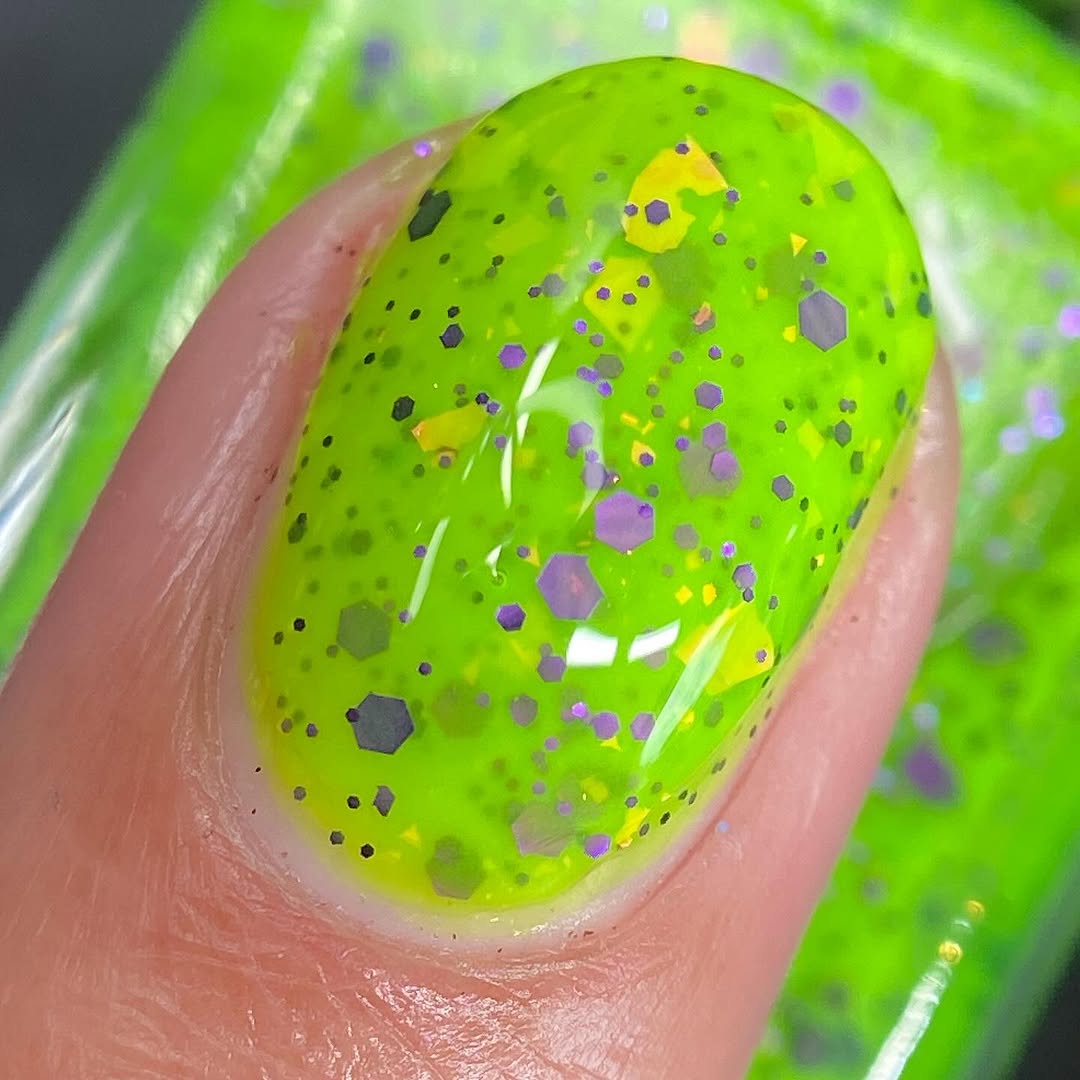 Dapper but no Dan by Cadillacquer, macro close-up of dense purple hexagonal glitter in varying sizes with yellow-orange iridescent diamond-shaped flakes on a neon lime green base