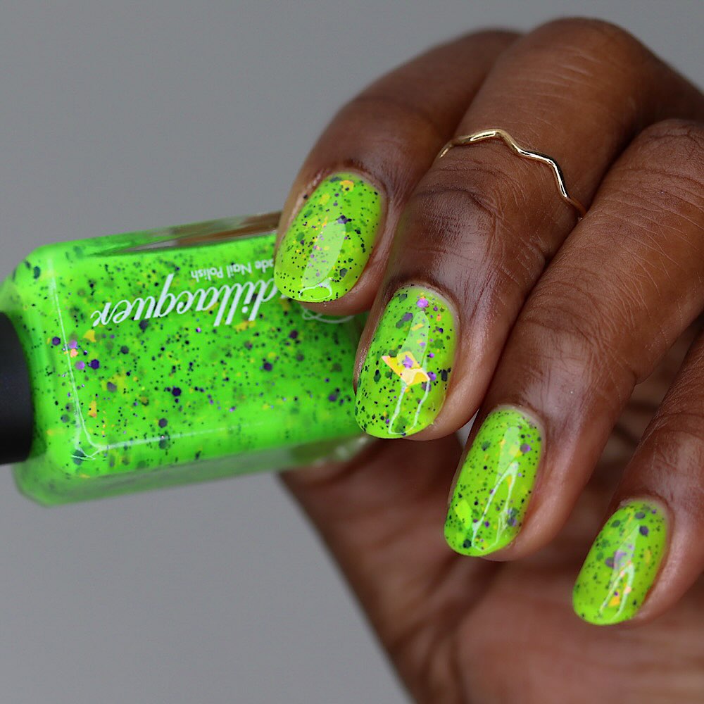 Dapper but no Dan by Cadillacquer, neon lime green with scattered purple glitter, orange-yellow iridescent flakes, and black speckles, bottle held in a rich hand