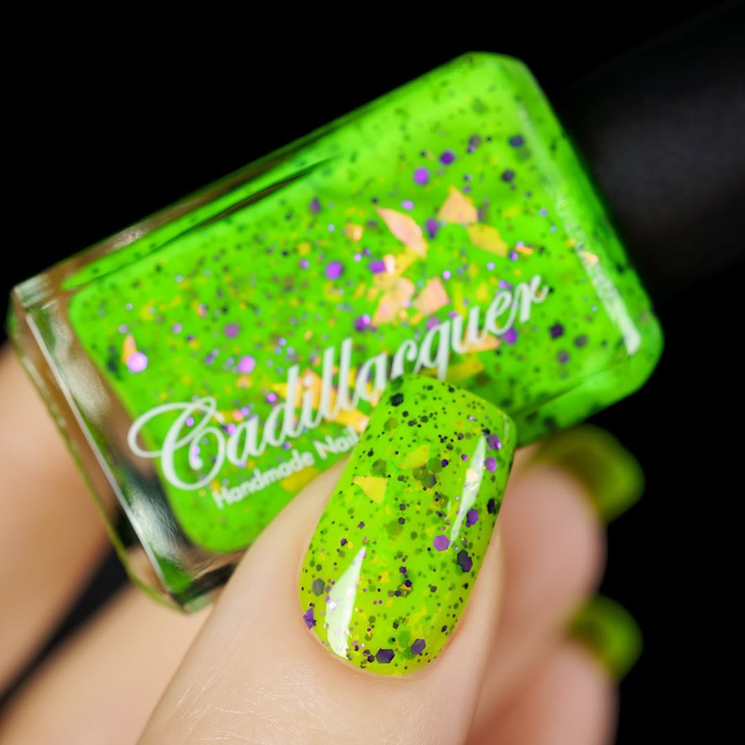 Dapper but no Dan by Cadillacquer, neon lime green with purple hex glitter and large orange-yellow iridescent flake particles, bottle held in a light hand