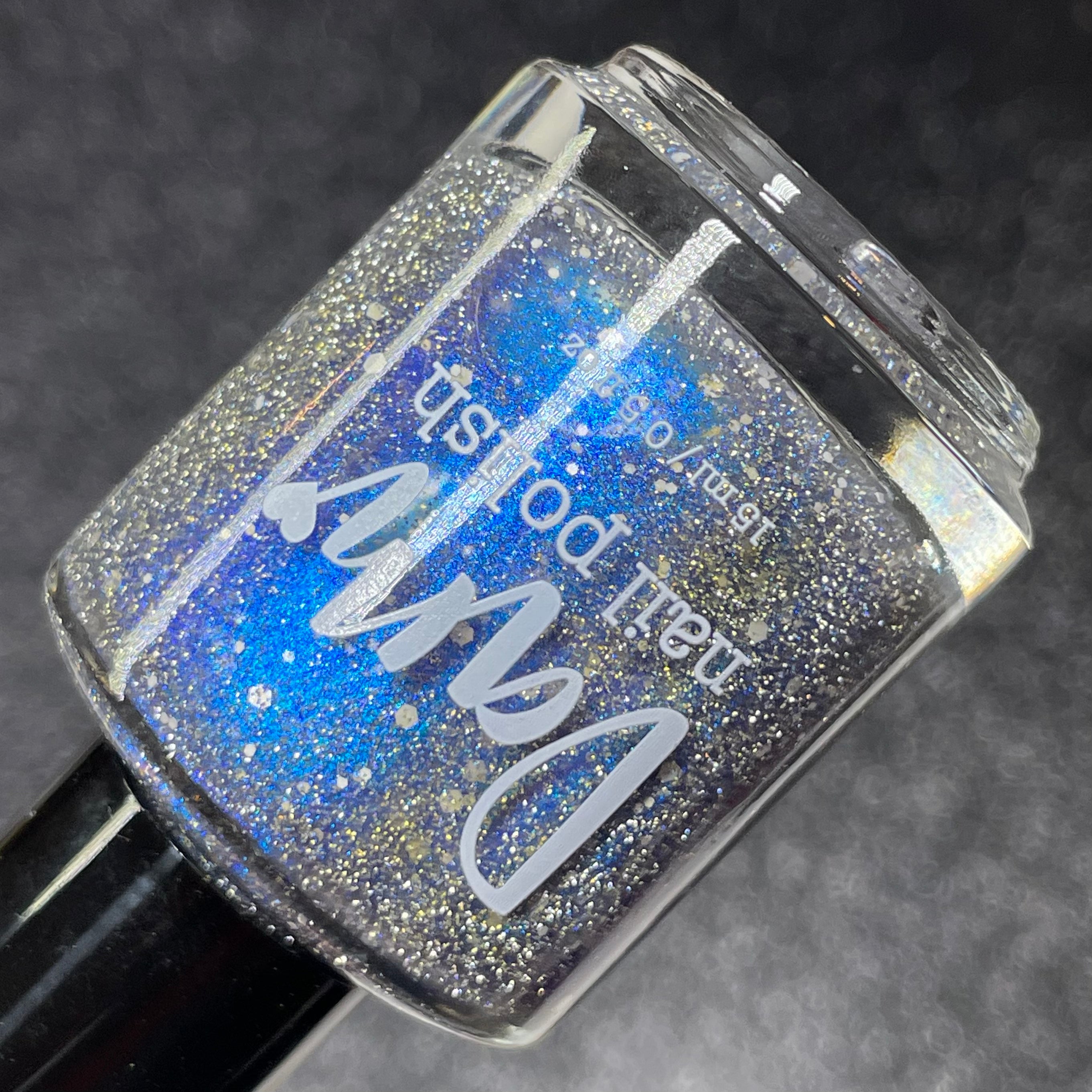 We're Off to See the Blizzard by Dam Nail Polish, black jelly base with blue-to-purple shifting shimmer and silver reflective glitter under direct flash, bottle standalone product shot