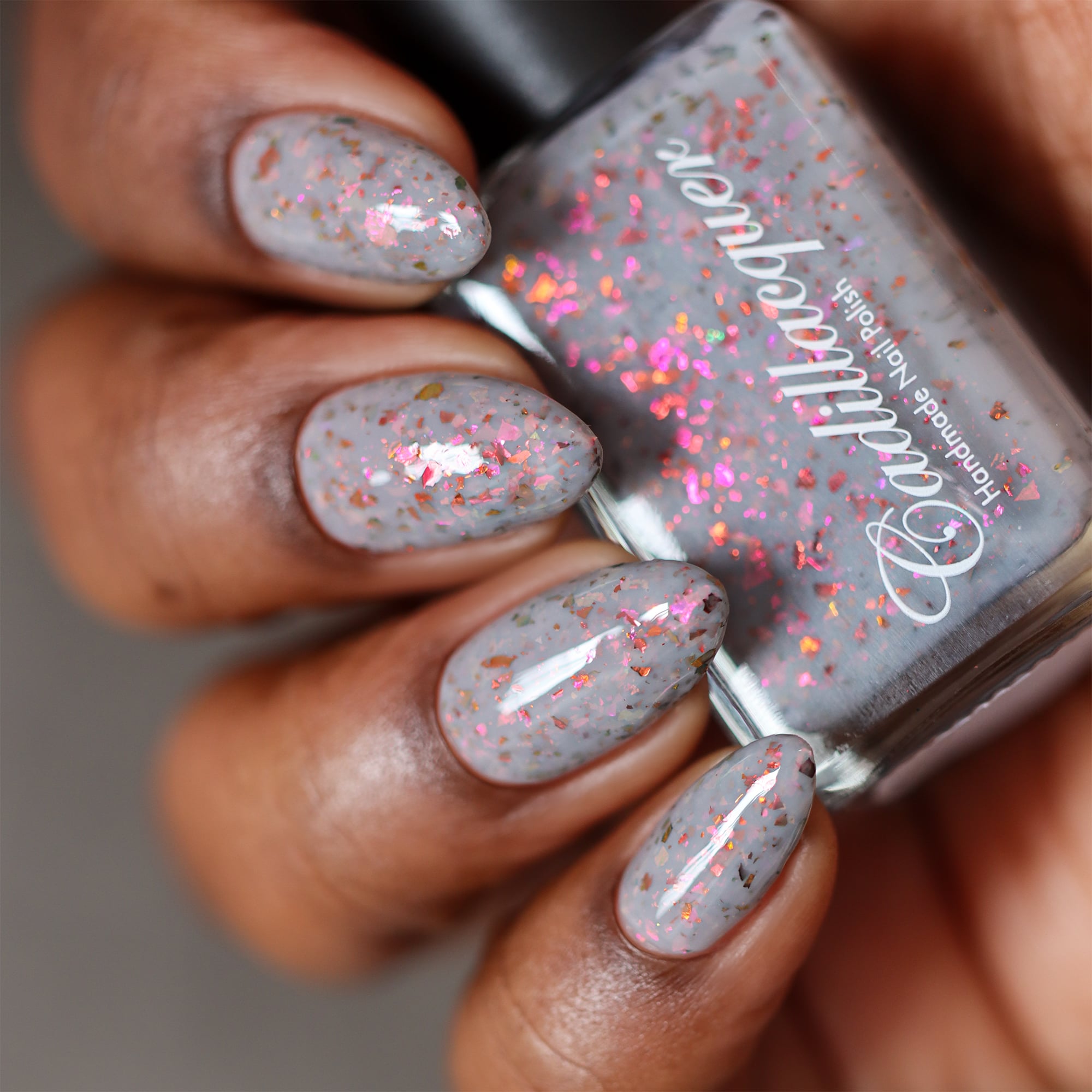 Cadillacquer Daydreaming grey red chameleon iridescent crelly nail polish, bottle held with four-nail swatch, rich skin, studio lighting