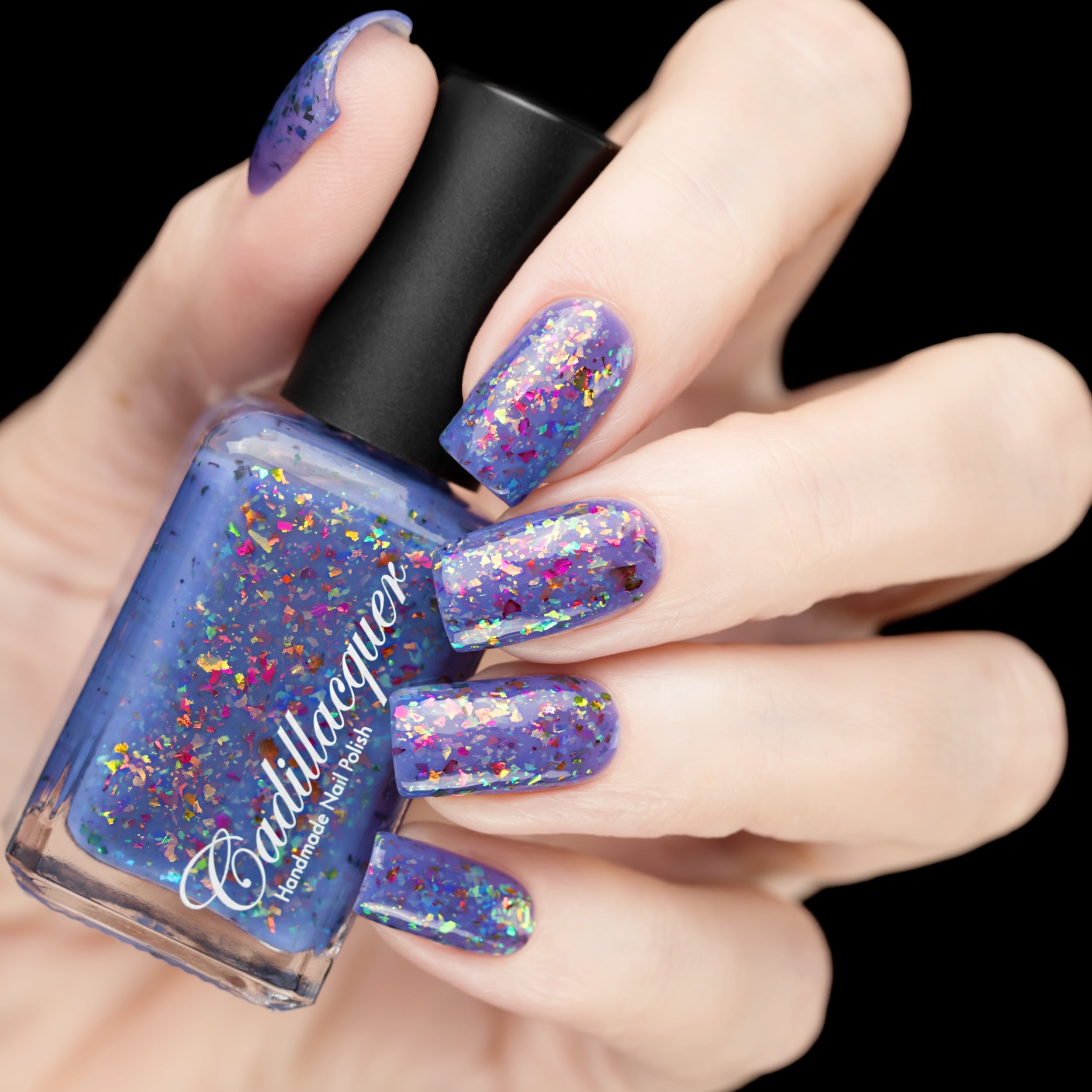 Cadillacquer Don't Worry purple pink chameleon iridescent crelly nail polish, bottle held with five-nail swatch, light skin, studio lighting