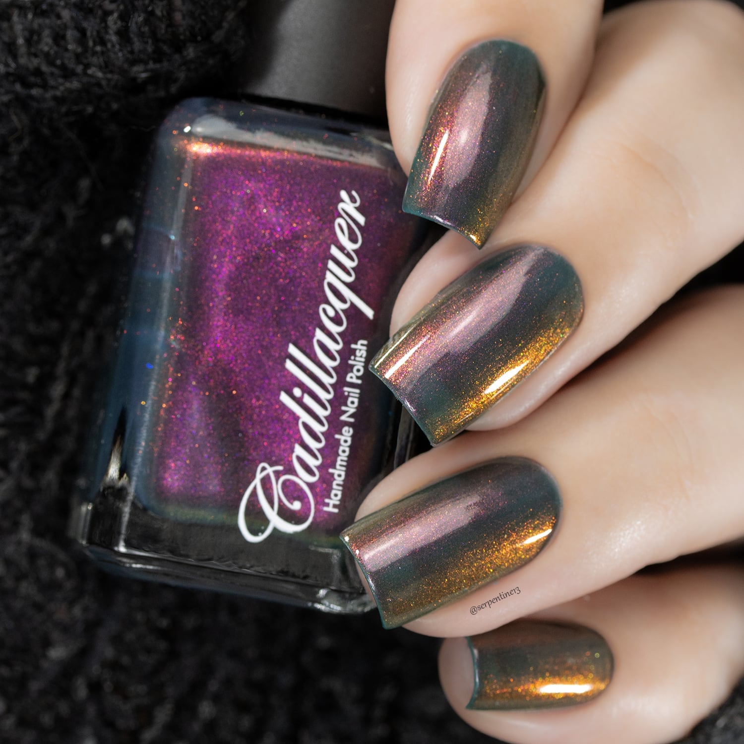 Multichrome shimmer Cadillacquer nail polish in Fear What You Will Become, showing a dark bottle with deep magenta-to-orange shimmer alongside five oval nails on light skin reading murky teal-grey base with a dramatic shift through amber-orange, dusty rose, and magenta shimmer depending on angle, shot under studio lighting, swatched by @serpentine13