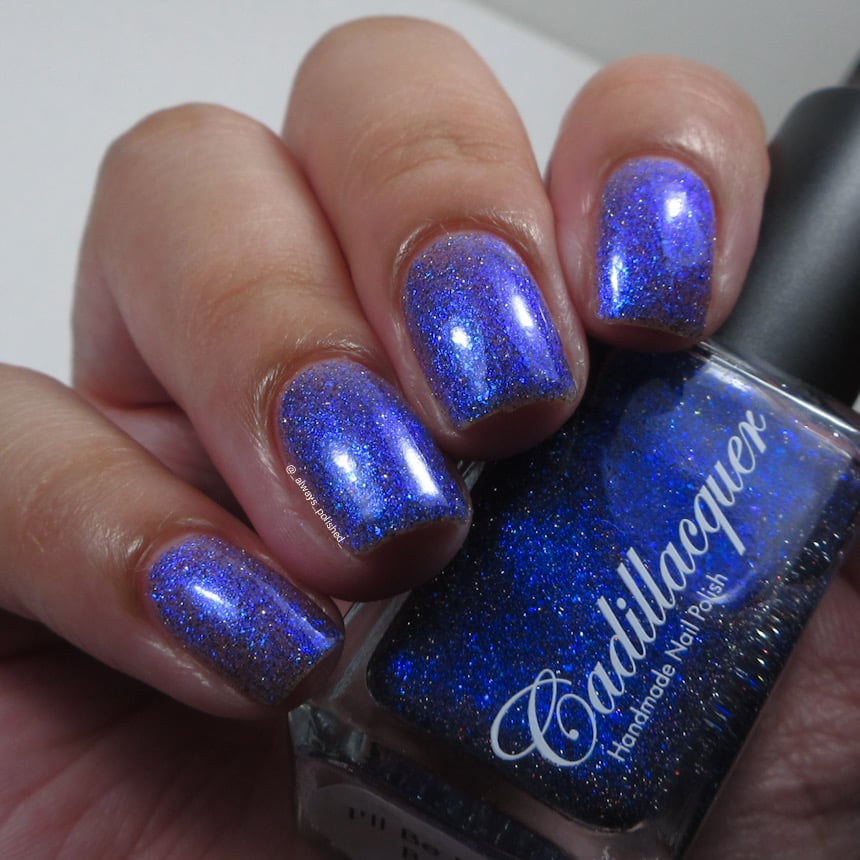 Shimmer, micro-flake and reflective glitter Cadillacquer nail polish in I'll Be Right Back, shown swatched on eight short natural nails held alongside the deep navy bottle, light-medium skin tone, indoor warm lighting, swatched by @_always_polished_