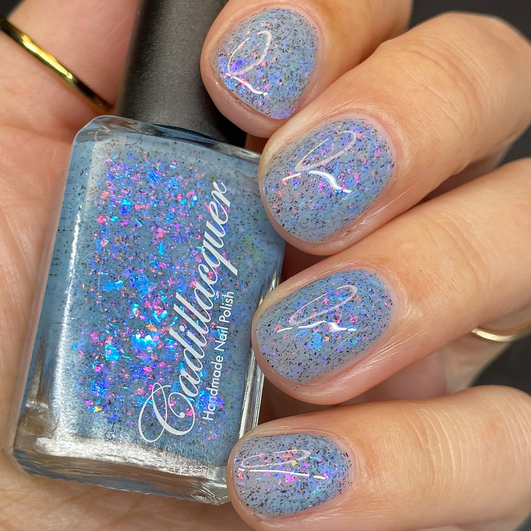 Cadillacquer Just Breathe pastel blue iridescent crelly nail polish, bottle held with four-nail swatch, light skin, studio lighting