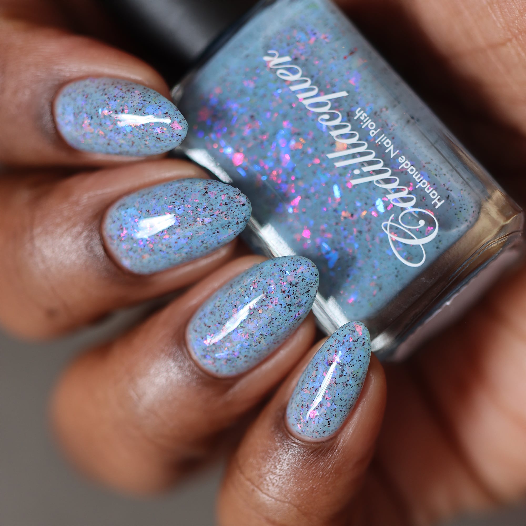 Cadillacquer Just Breathe pastel blue iridescent crelly nail polish, bottle held with four-nail swatch, deep skin, studio lighting