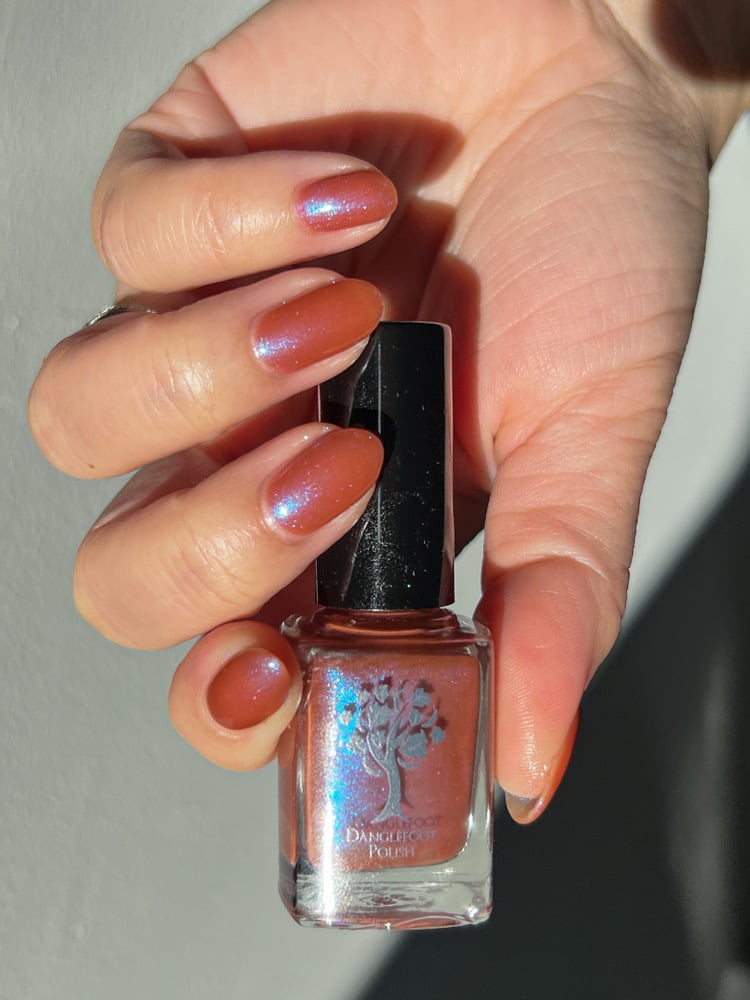 Enth E ND by Danglefoot Nail Polish, blue-brown shimmer bottle held in a light hand