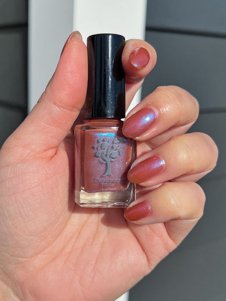 Enth E ND by Danglefoot Nail Polish, blue-brown shimmer bottle held in a light hand