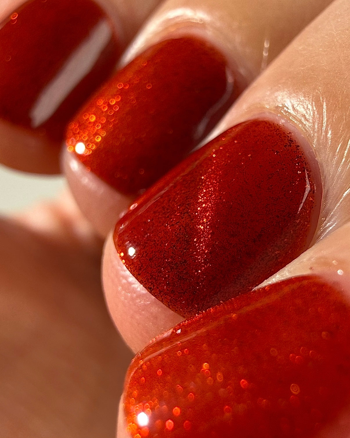 Stonewall by Glitch Lacquer, brick red jelly with bright red magnetic pigment, macro swatch on light skin tone