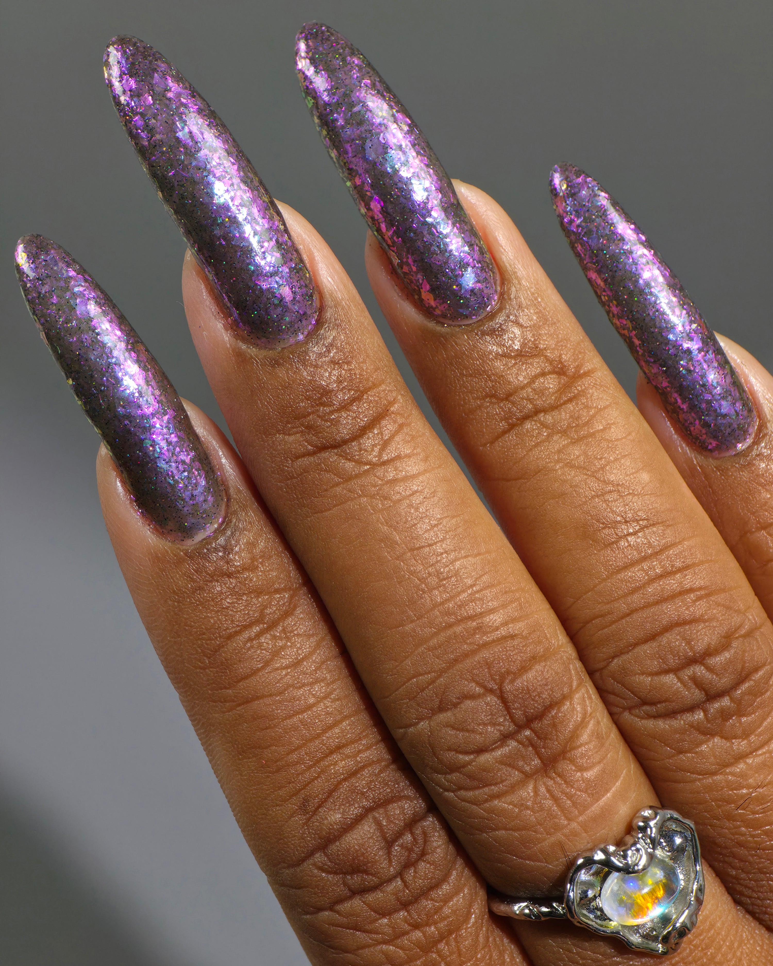 AVEN by Glitch Lacquer, soft black base, iridescent purple flakes, black holo micro-glitter, on deep skin tone almond nails