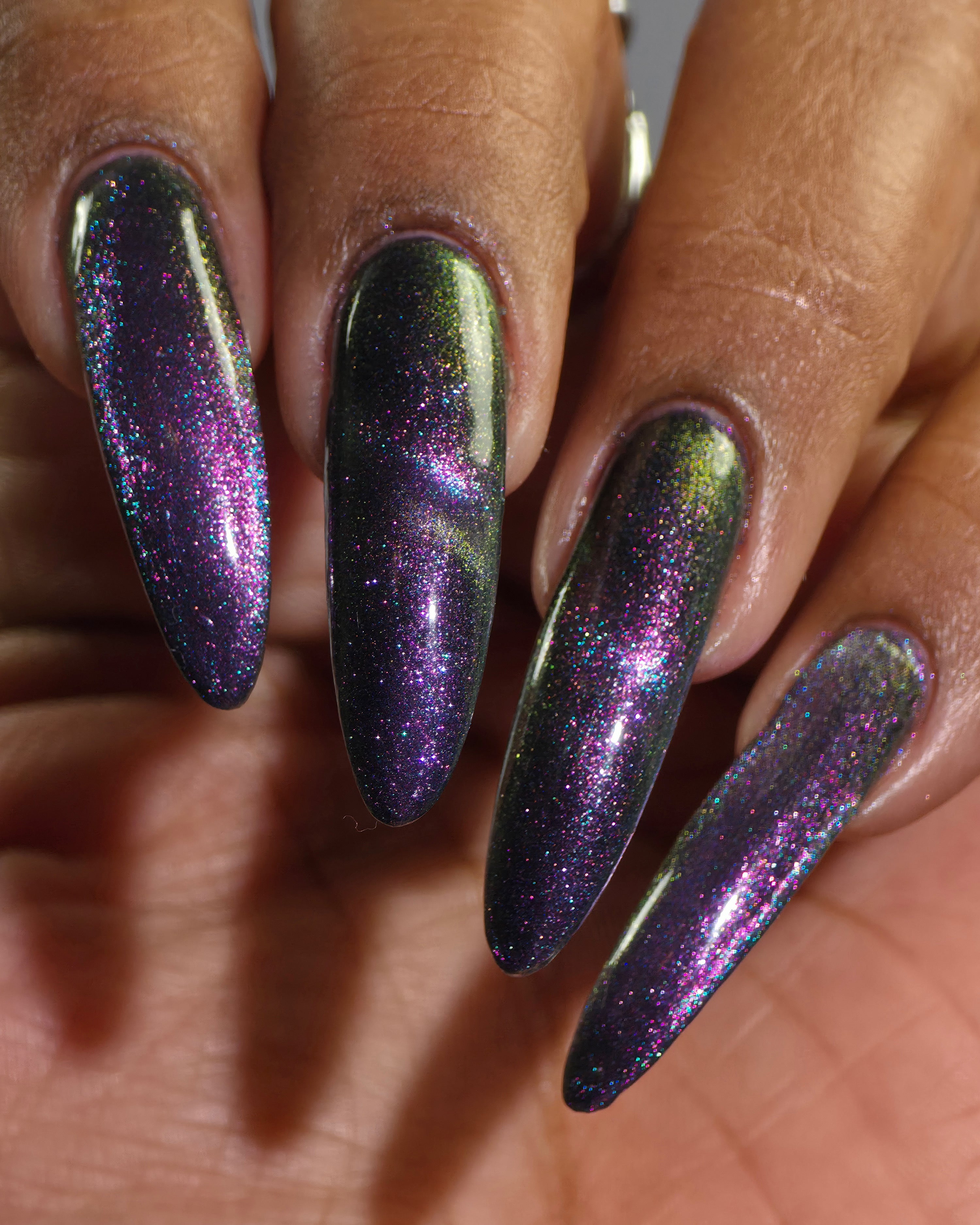 Lavender Menace by Glitch Lacquer, black jelly, purple sparkle, purple-blue magnetic, on medium-deep skin tone stiletto nails