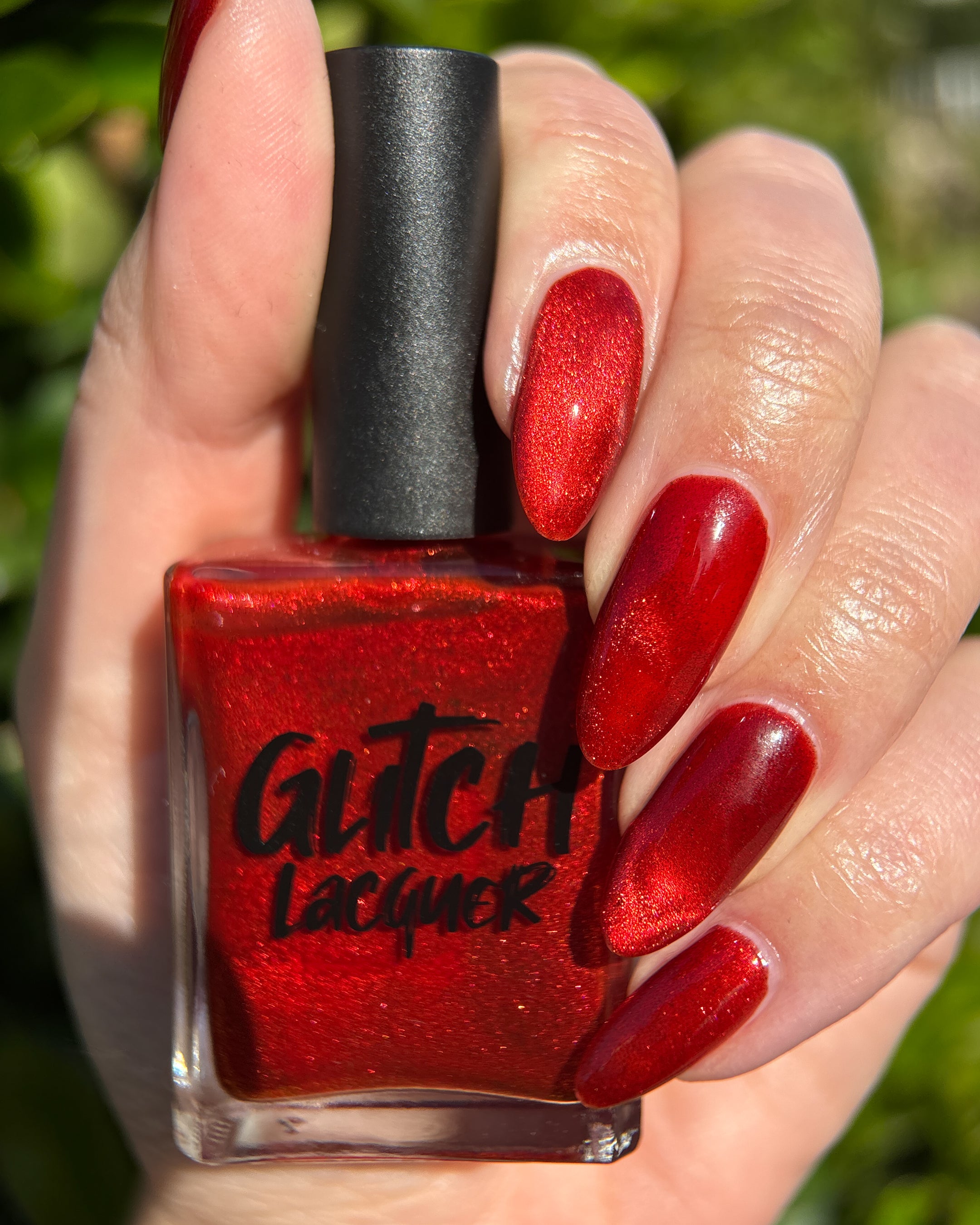 Stonewall by Glitch Lacquer, brick red magnetic jelly, bottle held with matching swatch on light skin tone