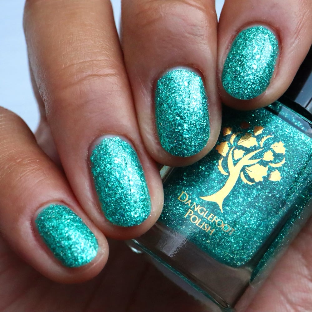 Mutant and Proud by Danglefoot Nail Polish, green-teal holographic reflective glitter flakie bottle held in a light-medium hand