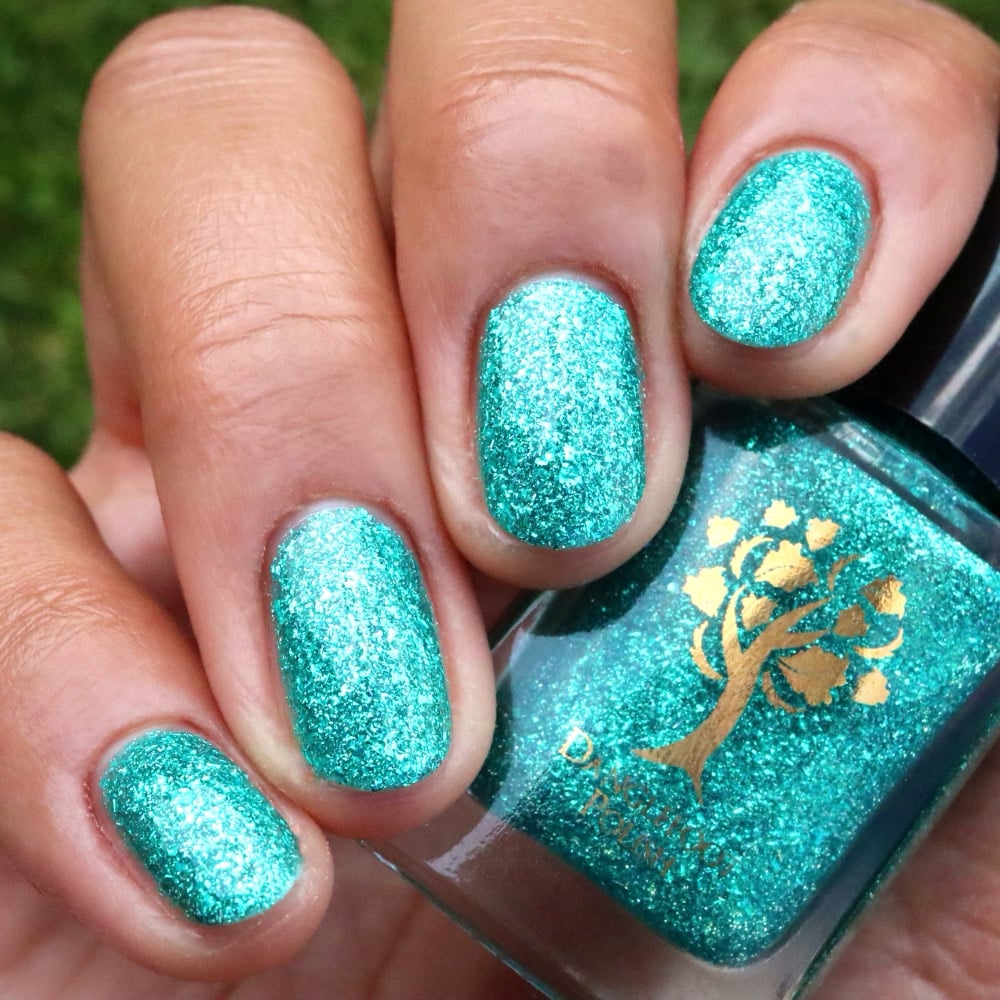 Mutant and Proud by Danglefoot Nail Polish, green-teal holographic reflective glitter flakie bottle held in a light-medium hand