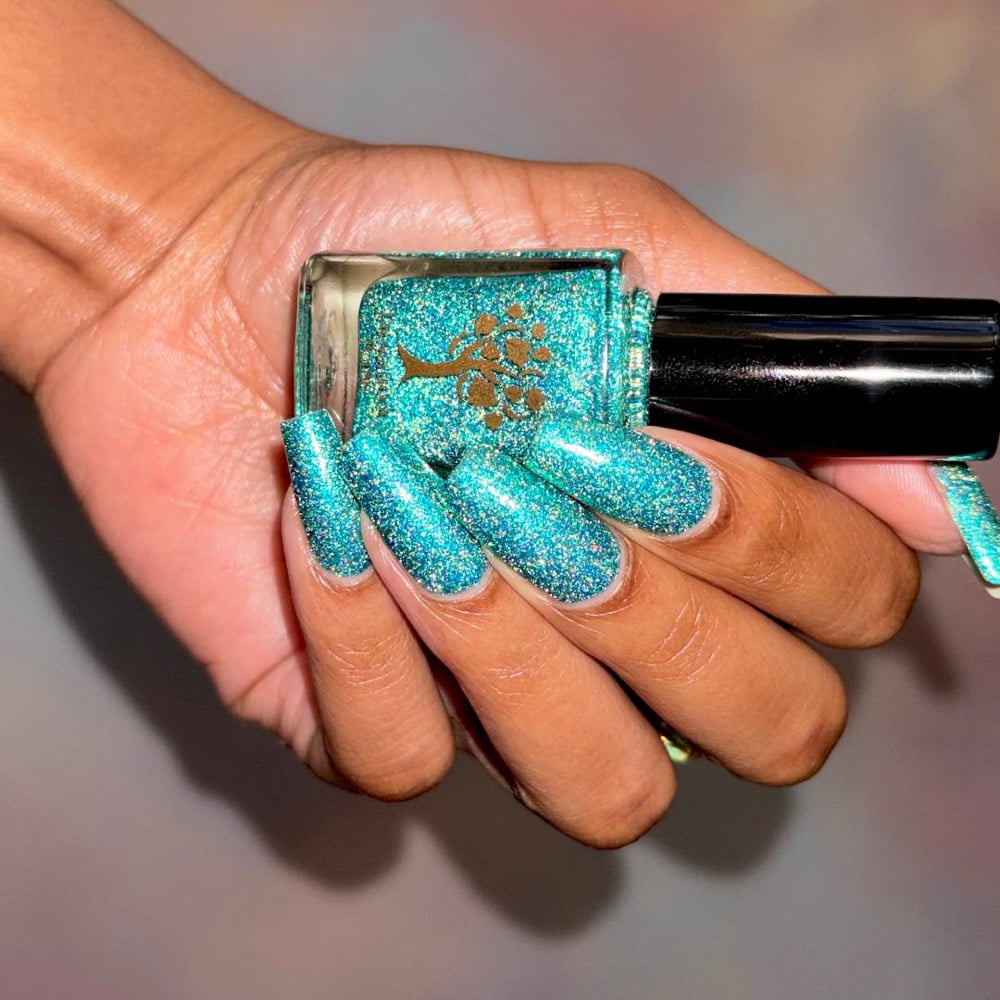 Mutant and Proud by Danglefoot Nail Polish, green-teal holographic reflective glitter flakie bottle held in a medium-deep hand