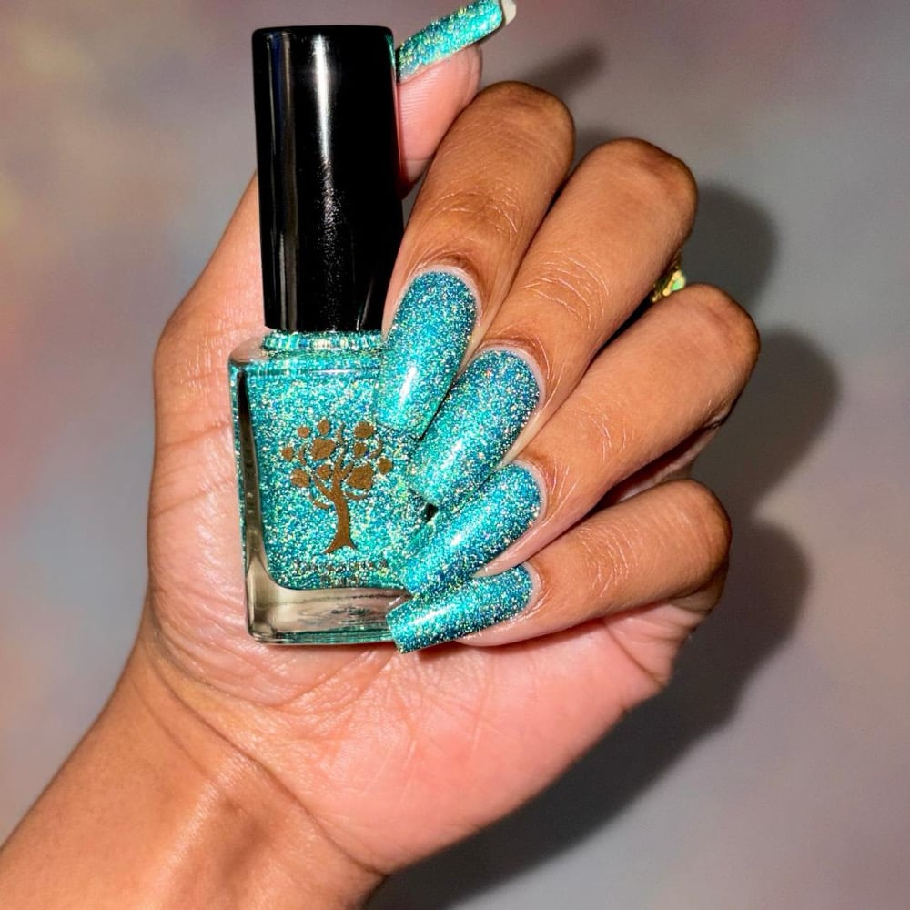 Mutant and Proud by Danglefoot Nail Polish, green-teal holographic reflective glitter flakie bottle held in a medium-deep hand