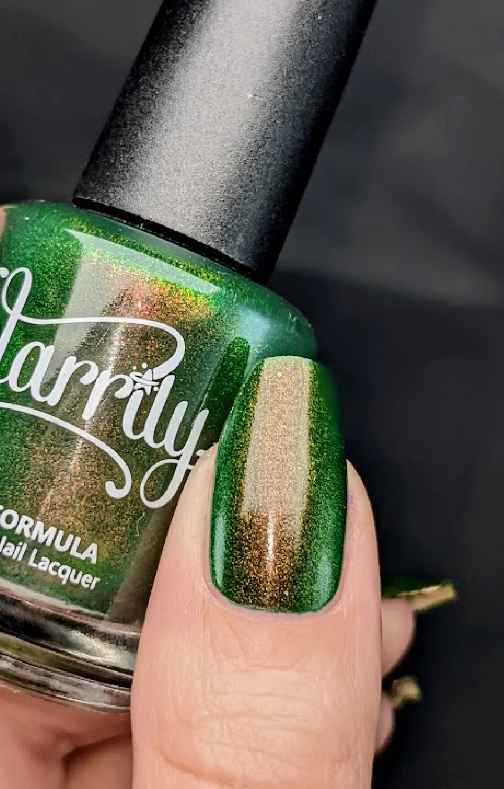 Artemis by Starrily, forest green shimmer with copper-bronze and gold shift under indoor warm light, bottle held in a light hand