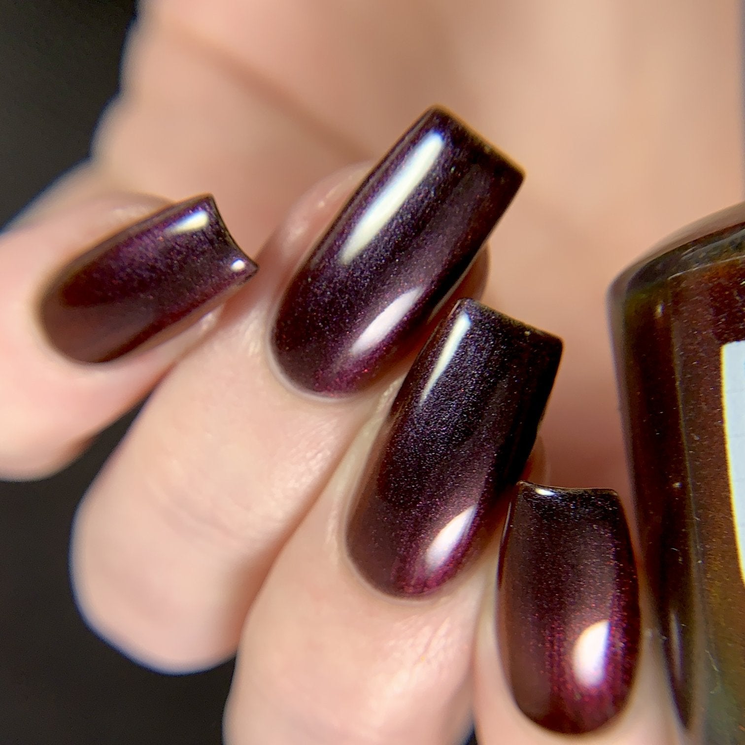 Change of Heart by Dam Nail Polish, blackened red multichrome with red-to-warm-brown color shift on four coffin nails, on a light skin tone hand