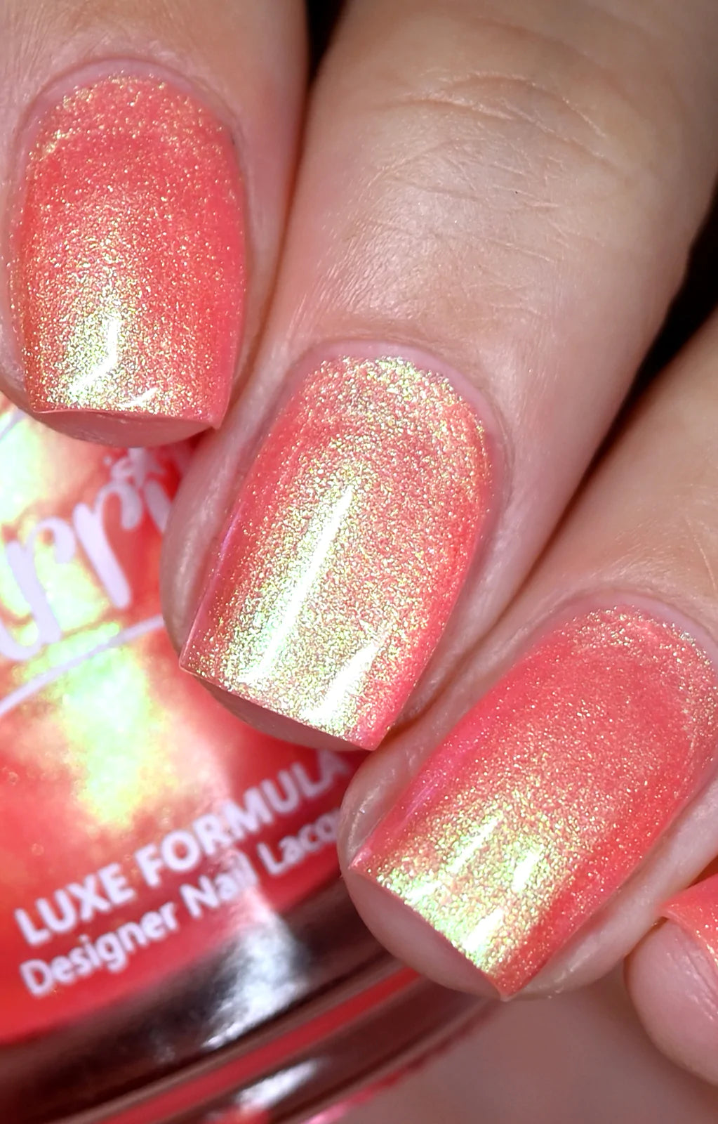 Nectar by Starrily, coral-salmon pink base with strong gold-green multichrome shimmer shift in bright daylight, on a light skin tone hand