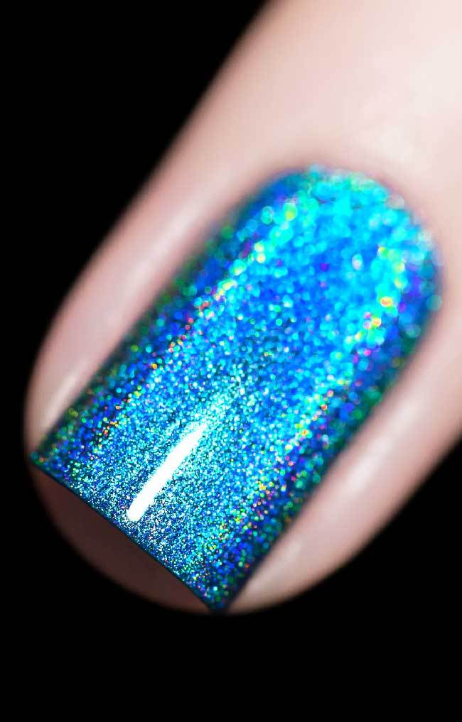 Cat Eyes by Starrily, medium blue linear holographic with intense cyan and green rainbow scatter under direct flash, on a light skin tone hand
