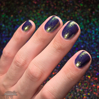 Sandman by Dam Nail Polish, deep blurple jelly with scattered gold-to-green multichrome shimmer in bright daylight, on a light skin tone hand