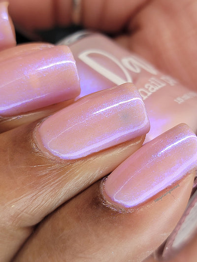 A Whimsical Dream by Dam Nail Polish, sheer blush pink base with dense blurple shimmer glowing violet under direct flash, on a medium skin tone hand