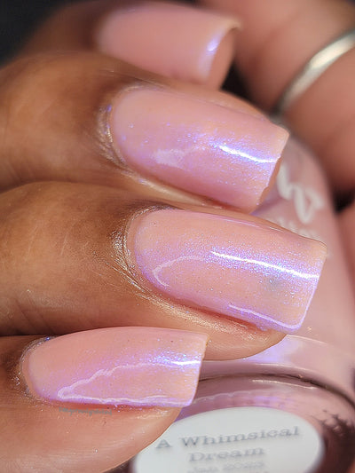 A Whimsical Dream by Dam Nail Polish, sheer baby pink base with glowing blurple shimmer pooling into violet-blue highlights in daylight, on a medium-deep skin tone hand