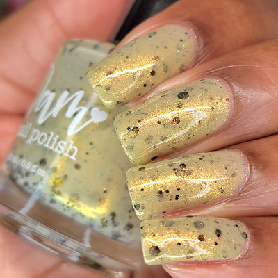OG Devo-tea by Dam Nail Polish, warm tan-yellow crelly with gold shimmer intensity highlighted in daylight, bottle held in a medium skin tone hand