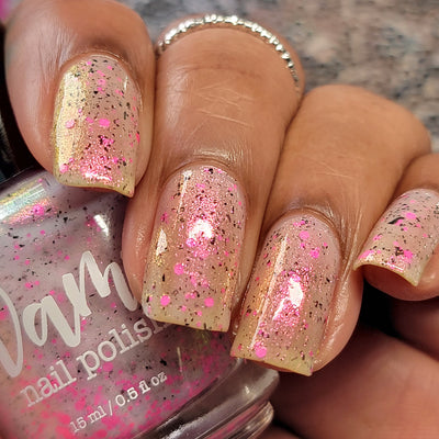 Shimmer Storm by Dam Nail Polish, sheer ivory-champagne base with gold flakes and dense neon pink circle glitters, on a medium skin tone hand