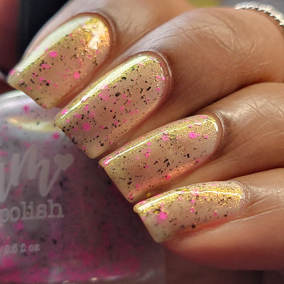 Shimmer Storm by Dam Nail Polish, sheer warm white base with gold shimmer shift and neon pink and black glitter particles, on a light-medium skin tone hand