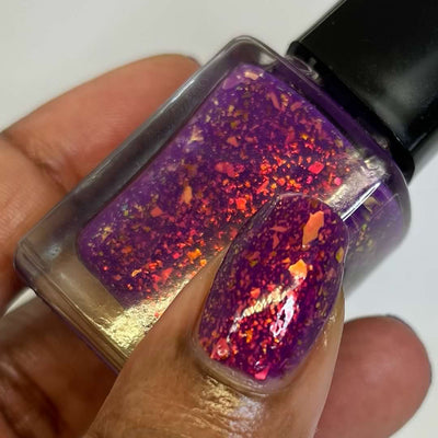 Evening in Provence by Chamaeleon Nails, red-orange and copper-gold multichrome flakies in jelly base, bottle held in a medium-deep hand