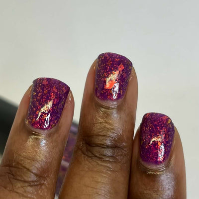 Evening in Provence by Chamaeleon Nails, deep magenta-purple jelly with orange-red and copper-gold UCC flakies under warm indoor light, on a rich skin tone hand