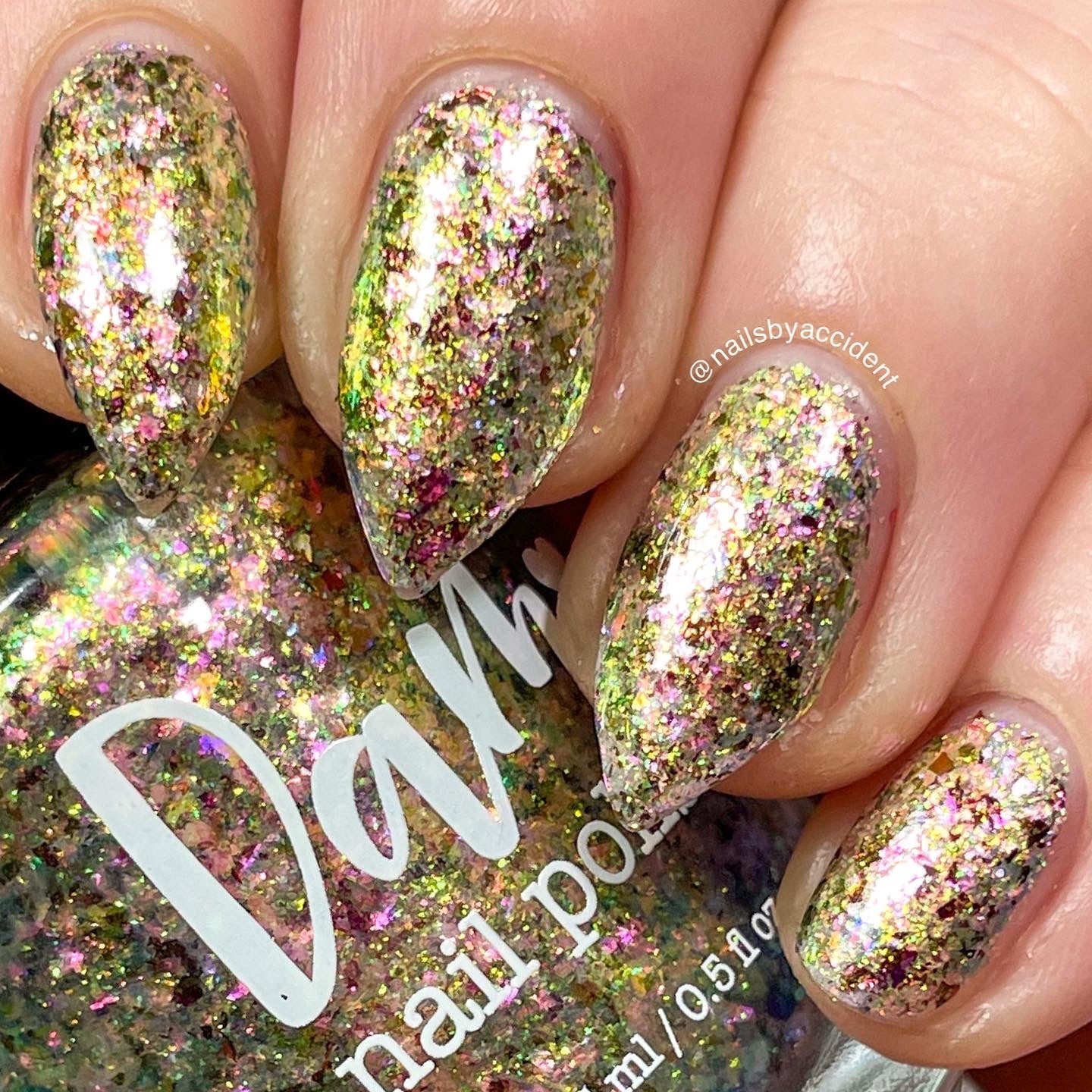 Ayla the Scoliosis Dolphin by Dam Nail Polish, multichrome flakie with scattered gold, pink, and yellow-green shifting flake shards over a warm golden base, on a light skin tone hand