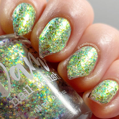 Ayla the Scoliosis Dolphin by Dam Nail Polish, multichrome flakie showing gold, teal, and green-shifting flakies over a sheer base under direct flash, on a light skin tone hand
