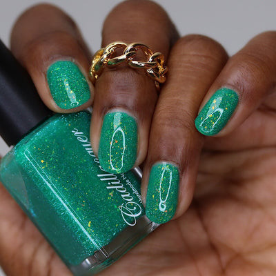 Blausee by Cadillacquer, teal green reflective glitter flakie crelly with yellow-green iridescent flakes and blue-green shimmer, bottle held in a rich hand