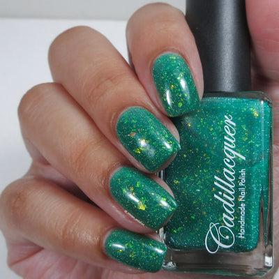 Blausee by Cadillacquer, teal green crelly loaded with yellow-green iridescent flakies and light teal reflective glitter in diffused daylight, bottle held in a light hand