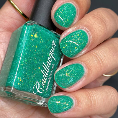 Blausee by Cadillacquer, teal green crelly with flake brightness intensified by direct flash, showing yellow-green iridescent flakes and fine reflective glitter scatter, bottle held in a light-medium hand