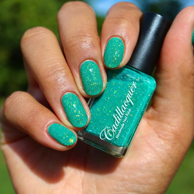 Blausee by Cadillacquer, teal green crelly with scattered yellow-green iridescent flakes and fine reflective glitter in bright outdoor daylight, bottle held in a light-medium hand