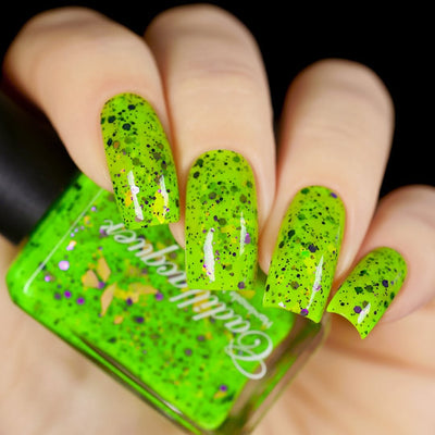 Dapper but no Dan by Cadillacquer, neon lime green crelly with black micro-glitter, purple hex glitter, and multichrome iridescent flakes, bottle held in a light hand