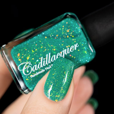 Blausee by Cadillacquer, teal green crelly with yellow-gold iridescent flakies and light blue reflective glitter under direct spot lighting, bottle held in a light hand