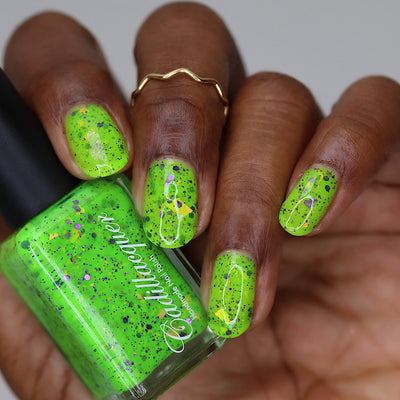 Dapper but no Dan by Cadillacquer, electric lime green with black micro speckles, purple hex glitter, and orange-yellow iridescent flakes, bottle held in a rich hand