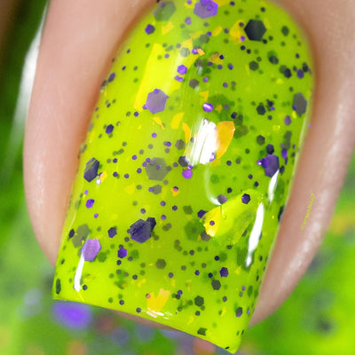 Dapper but no Dan by Cadillacquer, macro close-up of purple hexagonal glitter in varied sizes with orange-yellow iridescent flake shards on a neon lime green base