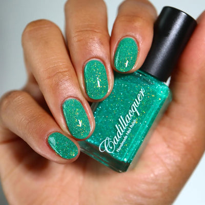 Blausee by Cadillacquer, teal green crelly with yellow-gold iridescent flakes and light blue reflective glitter, bottle held in a light-medium hand