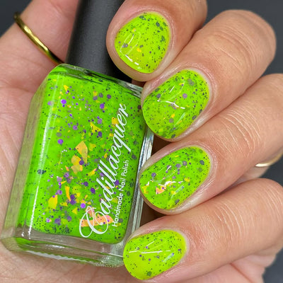 Dapper but no Dan by Cadillacquer, neon lime green jelly base with scattered purple hex glitter and large orange-yellow iridescent shards, bottle held in a light-medium hand