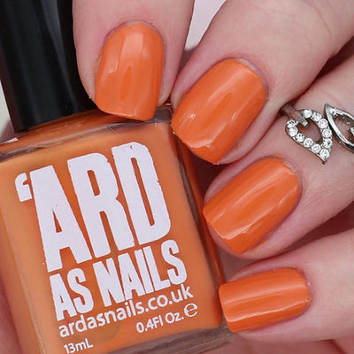 Sunset by 'Ard As Nails, warm orange creme with glossy finish, bottle held in a light hand