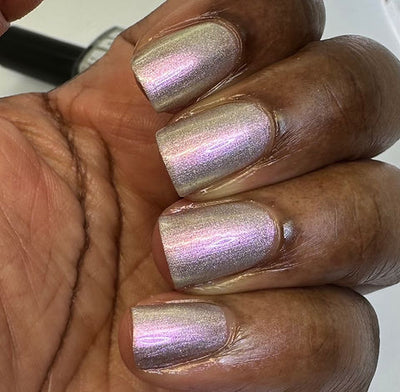 Blushing Bridesmaid by 'Ard As Nails, pink-to-green holographic duochrome shimmer topper with strong pink shift over warm champagne base under direct flash, on a deep skin tone hand