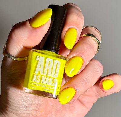 Lightning Speed by 'Ard As Nails, high-voltage neon yellow creme in bright daylight, bottle held in a light skin tone hand